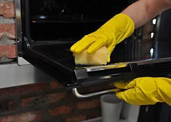 Gloved hands cleaning the inside of an oven door