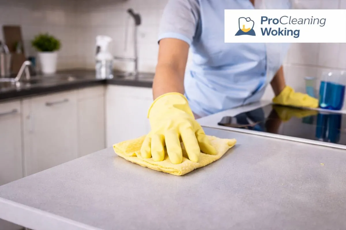 Gloved hand wiping a grey kitchen worktop with a yellow cloth