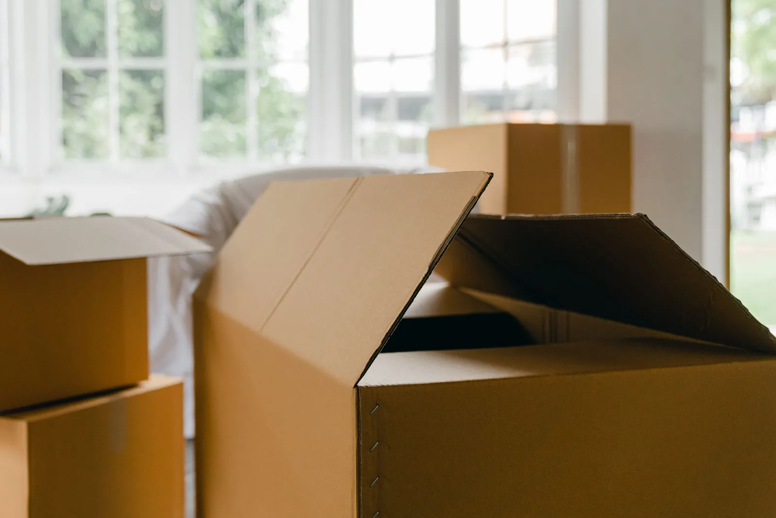 Open cardboard moving boxes in a bright room with large windows