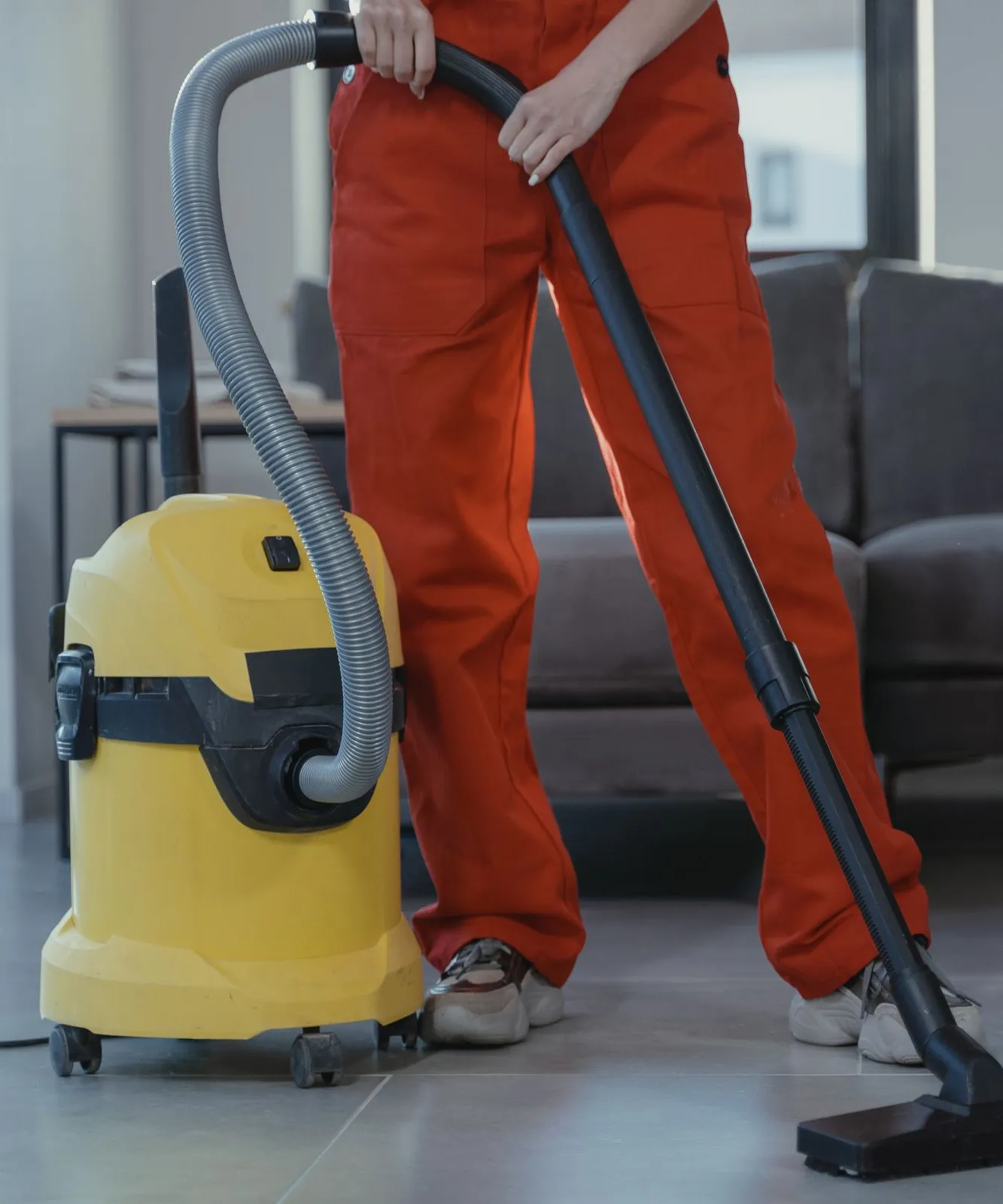 A person in red overalls vacuuming a living room floor